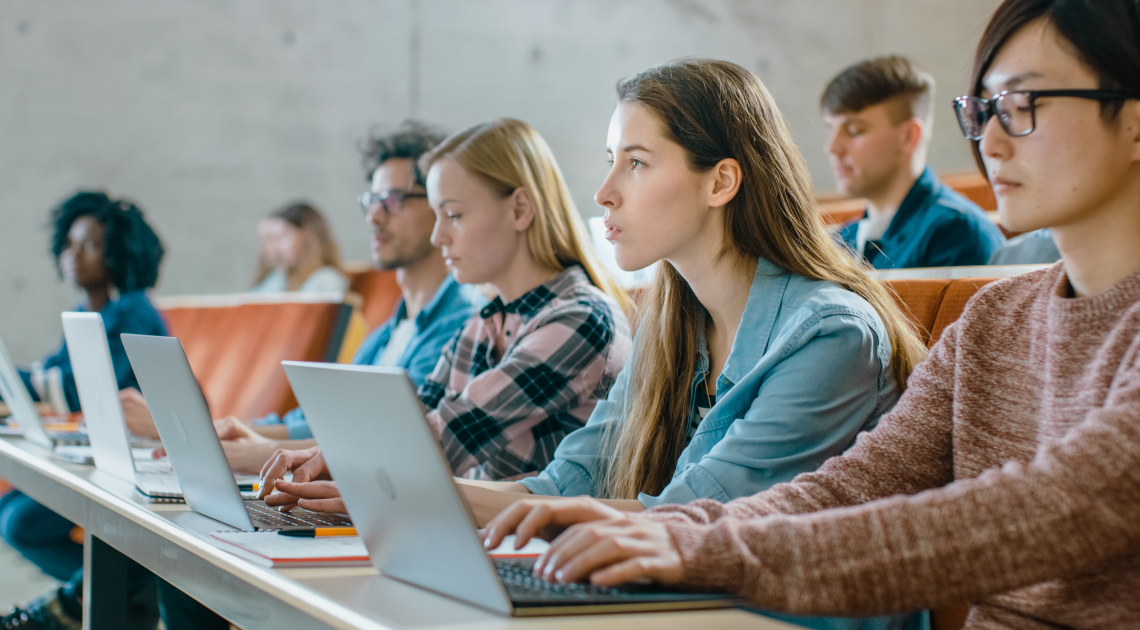 Studentinnen und Studenten sitzen mit Laptops in einem Hörsaal